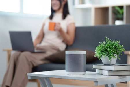 Smart Home. Woman enjoying coffee while using laptop near smart speaker.の写真素材