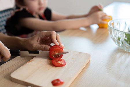 A woman is cutting a tomato on a wooden cutting board