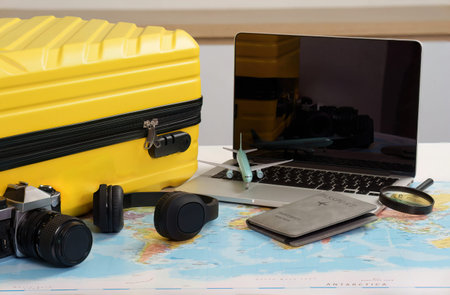 Travel Essentials. Yellow suitcase, laptop, and camera on world map.