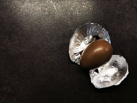 Easter chocolate egg with a foil on a black tableの写真素材