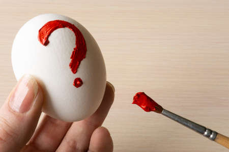 a person draws a red question mark on a white egg