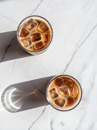 Two glasses of iced coffee with ice cubes on a white marble surface, realistic style, top view, concept of refreshing summer beverageの写真素材