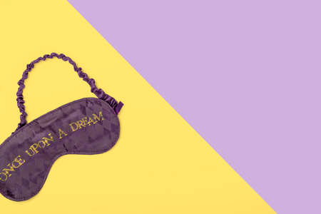 Purple satin  sleeping mask on yellow and purple background with space for text. Minimal flat lay...