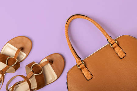 Flat lay of female fashionable leather handbag and sandals on pastel violet backgroundの写真素材