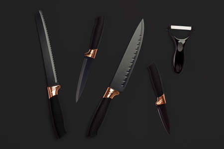 Top view on  black kitchen knives and peeler set on black background