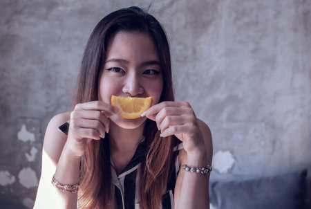 Portrait of an asian beautiful woman is smiling and holding a piece of orange with copy space on the right sideの写真素材