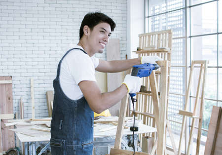 An asian carpenter using drill machine to make a hold on woodの写真素材