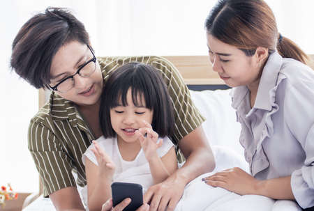 A warm family spending time together at home in holiday. The little girl is studying online by using mobile phone.の写真素材