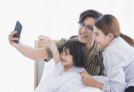 An asian family spending time and taking picture together in bedroomの写真素材