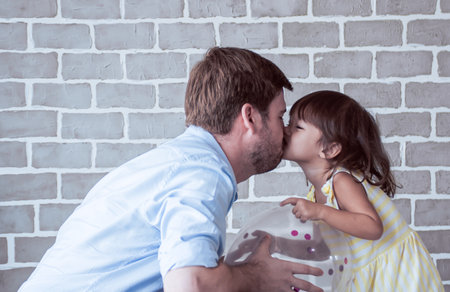 A caucasian father is kissing his little dautghter and playing together at homeの写真素材