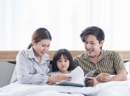 Asian dad and mom are reading bedtime stories to their daughter before sleepingの写真素材