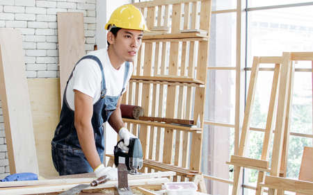 An asian carpenter using drill machine to make a hold on wood