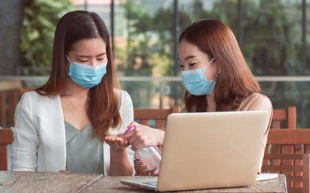 Two asian business women wearing mask and washing hands by gel before working. New Normal and Business Concept.の写真素材
