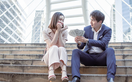 Asian man giving a lot of money to his girlfriend. Business Concept.の写真素材