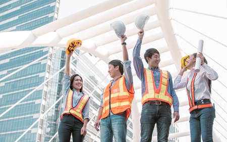 Portrait of engineering group wearing uniforms and holding safety helmets while standing outside near buildings. Construction Concept.の写真素材