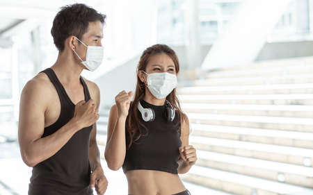 Asian sportive man and woman wearing face mask to protect virus and doing exercise by running or jogging outdoor in the morning. Health and Sport Concept.の写真素材