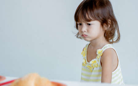 A little caucasian girl is eating bread for breakfast in the morning. There is white copy space on the left side. Education and Children Concept.の写真素材