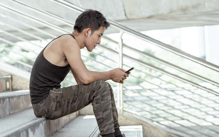 Portrait of Asian handsome man sitting on steps outside and chat by using mobile phone