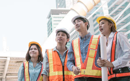 Portrait of engineering group wearing uniforms and safety helmets while standing outside near buildings. Construction Concept.の写真素材