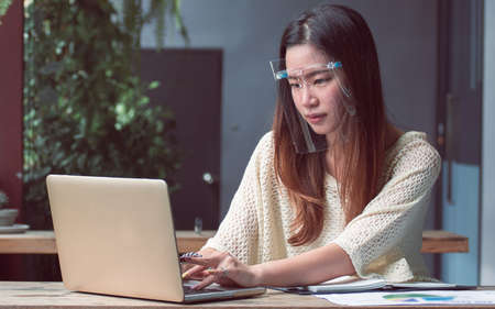 Asian beautiful woman wearing mask to protect virus  and using mobile phone and laptop for working...