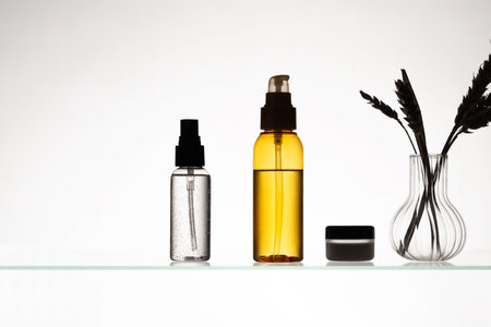 Different cosmetic products on a glass shelf on white background. Mockup of skincare and bath products on a glass shelf. Dispensers and tubes with beauty productsの写真素材