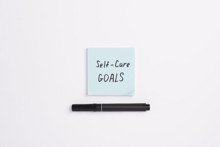 Paper note with words 2025 Self Care Goals and black marker on a white minimal background. Concept of goals and plans for the new year. Concept of mental health care, top view, copy spaceの写真素材