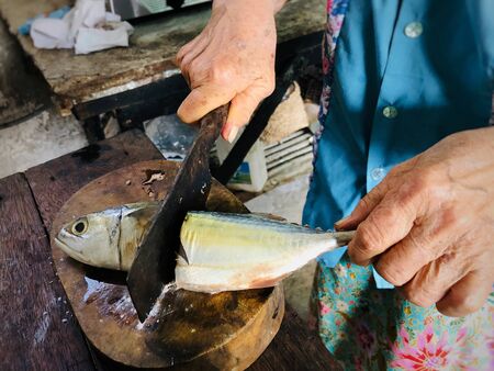 old woman hands cut fish with knife on wooden cutting board