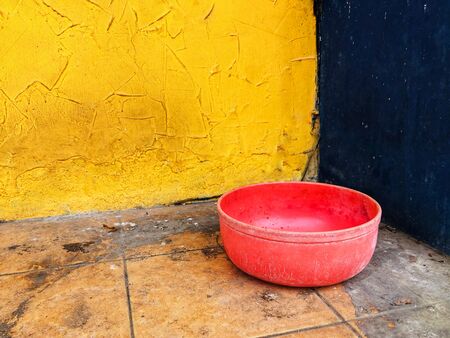 Red bowl at yellow and dark blue corner of building on dirty orange floorの写真素材