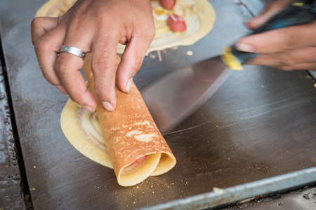 Seller rolling Khanom Tokyo thin flat pancake filled with sweet custard cream,pork,sausage.It is a Thai street snackの写真素材