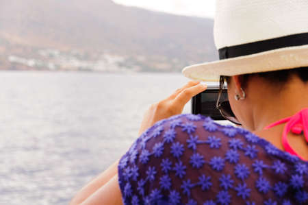 A tourist takes a picture on a canal with a boat. In the background an island and the seaの写真素材