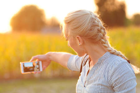 A young blond woman makes a selfie in the setting sunの写真素材