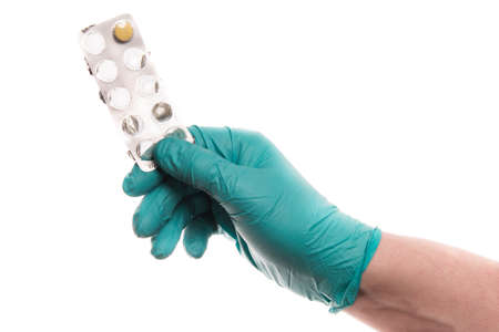 A hand of a man in a green latex glove hold a strip of pills isolated on a solid white background