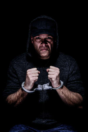 White male wearing baseball hat and hood, sit handcuffed on a chair. grunge styleの写真素材