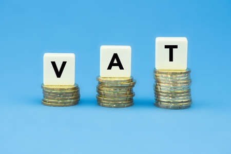 VAT (Value Added Tax) on stacks of gold coins over blue backgroundの写真素材