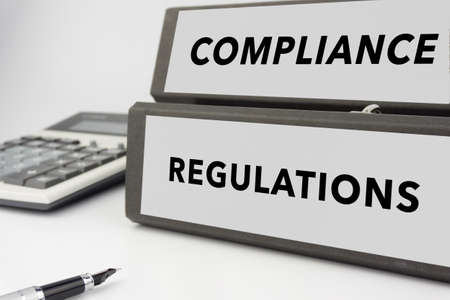 Compliance and Regulations - two binders on white background with calculator and pen