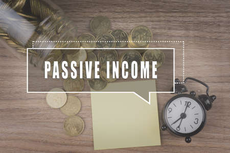 Coins spilling out of a glass jar on wooden background with PASSIVE INCOME text . Financial Conceptの写真素材