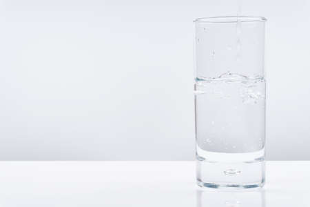 Pouring water into glass from a bottle, on white background.の写真素材