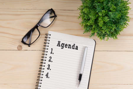 Office workplace with glasses and plant. Notebook with agenda on wooden table from above, planning and design concept.の写真素材