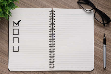 Notebook with blank checklist on wooden table with plant and glasses.の写真素材