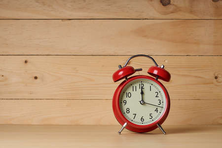 Old red alarm clock, Red alarm clock shows to 12 oâclock on wood table with wooden background.の写真素材