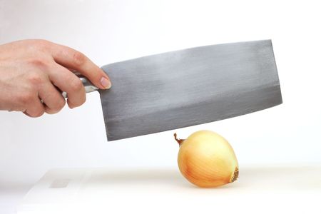 A stainless steel cleaver poised to chop a fresh whole raw onion on a cutting boardの写真素材