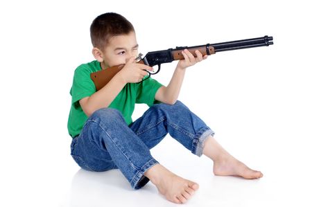 six-year-old boy aiming a toy rifle, in sitting position, isolated on whiteの写真素材