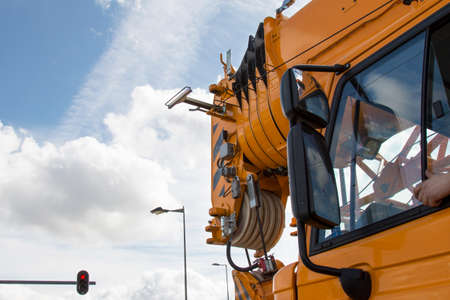 During a stop at a red traffic light crane driver stuck his arm out the window, a huge mirror machine, a red arrow on a traffic light, the clouds in the sky, clear dayの写真素材