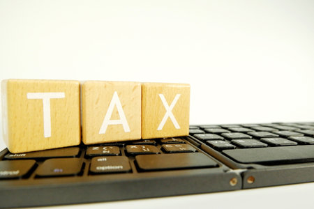 Wooden cubes with the word TAX on the keyboard of a laptopの写真素材
