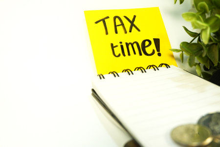 Tax time text on yellow sticky note with coins and plant on white backgroundの写真素材