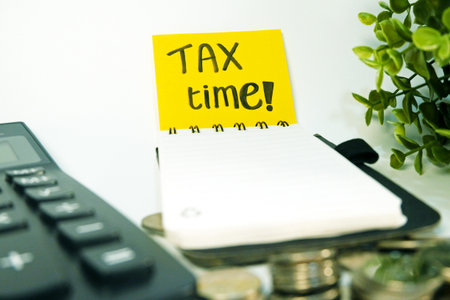Tax Time text on sticky note with coins and calculator on white backgroundの写真素材