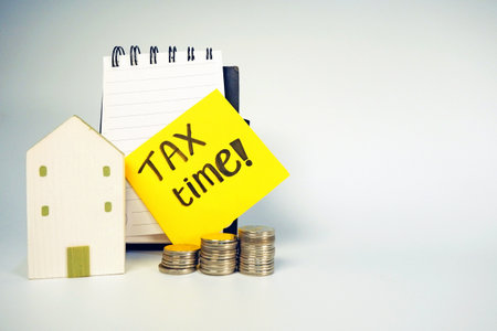 Tax time concept. Miniature house and coins with text TAX TIME.の写真素材