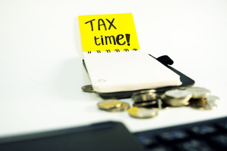Tax time text on sticky note with coins and laptop on white background digitally created stock photoの写真素材