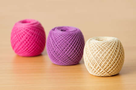 Balls of threads on a wooden table.  Three multicolored tangle of yarn.