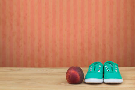 Green sneakers and a peach on a wooden table and red grunge wallpaper with stripes. Space for textの写真素材